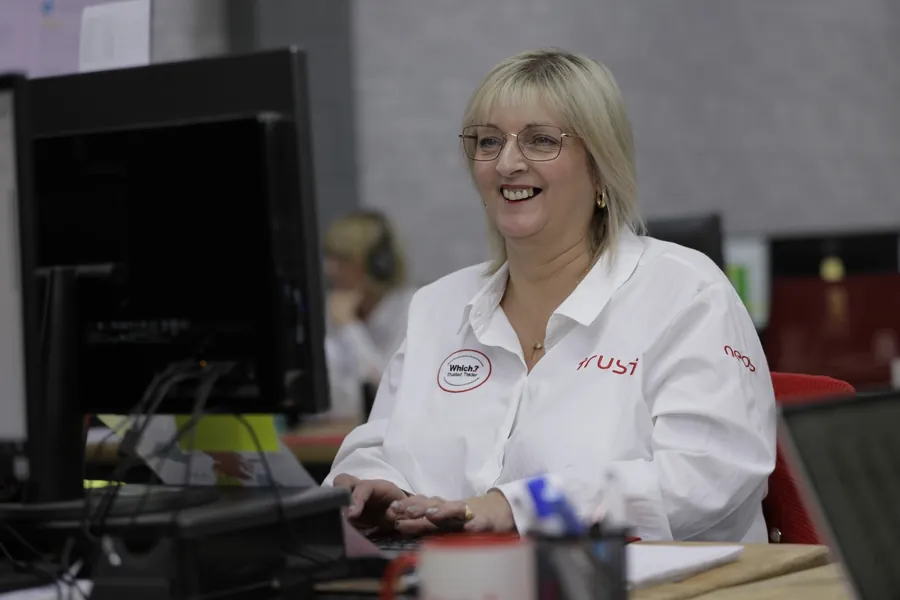 A Trust customer adviser smiling at her desk, with the team taking calls behind her