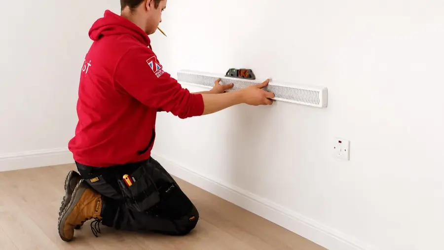 A Trust engineer levelling a slim radiator against the wall during an install
